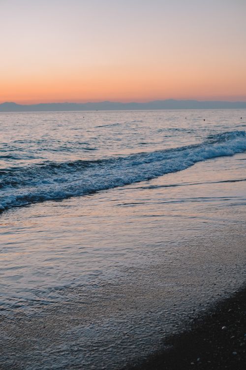 Free Beautiful sunset over a tranquil beach, highlighting the calm ocean waves on the shoreline. Stock Photo