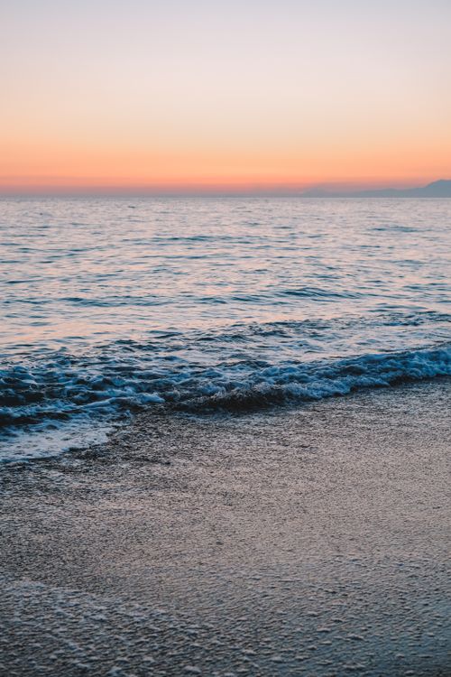 Free A peaceful sunset cast over gentle ocean waves at a sandy beach, perfect for relaxation. Stock Photo