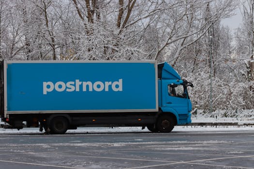 A blue PostNord truck parked in a snowy winter setting, showcasing transportation in cold environments.