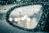 汽车后视镜上的雨滴映出路灯光，呈现出水的纹理和散景效果