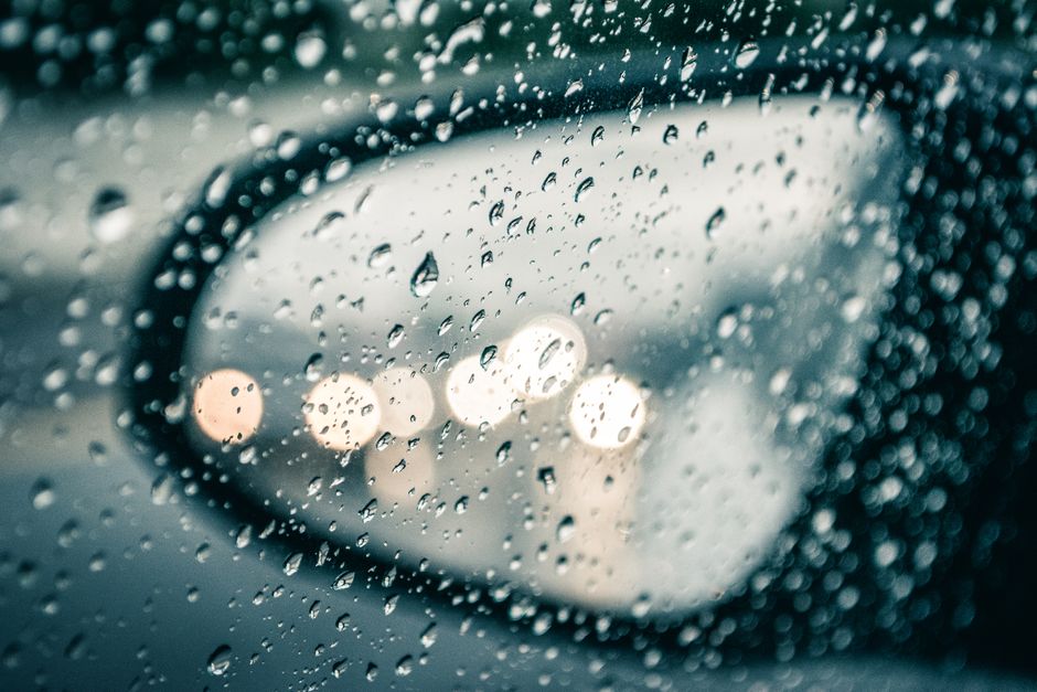Raindrops on a car mirror reflecting street lights, showcasing water texture and bokeh effects.