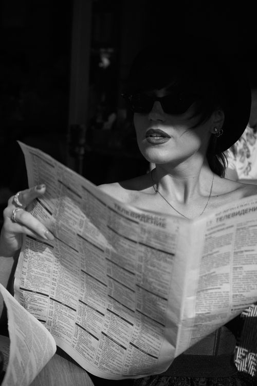 Free Elegant woman in sunglasses reading a newspaper, captured in a black and white portrait, showcasing vintage style. Stock Photo