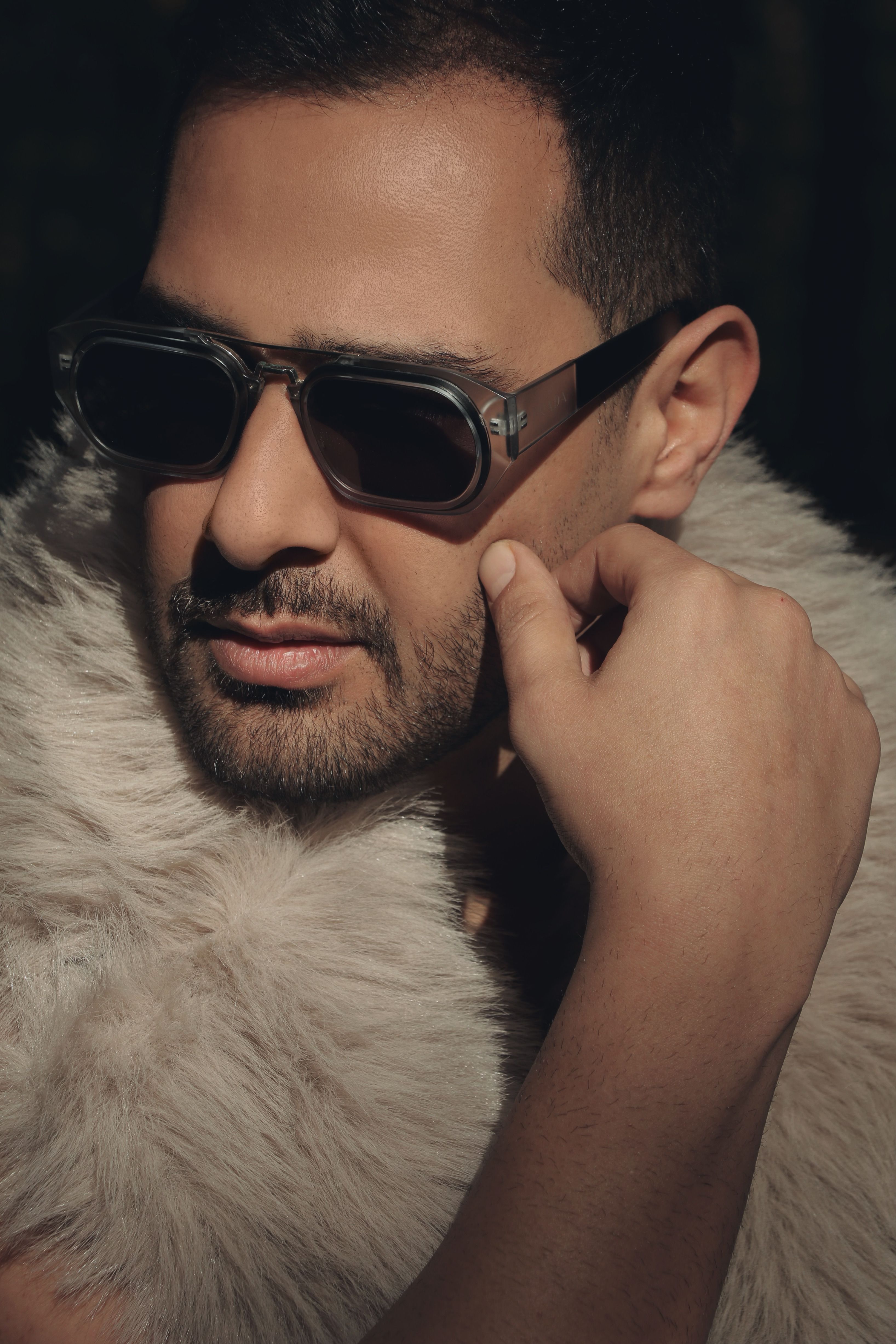 Portrait of a fashionable man in sunglasses and fur scarf, exuding mystery and style.