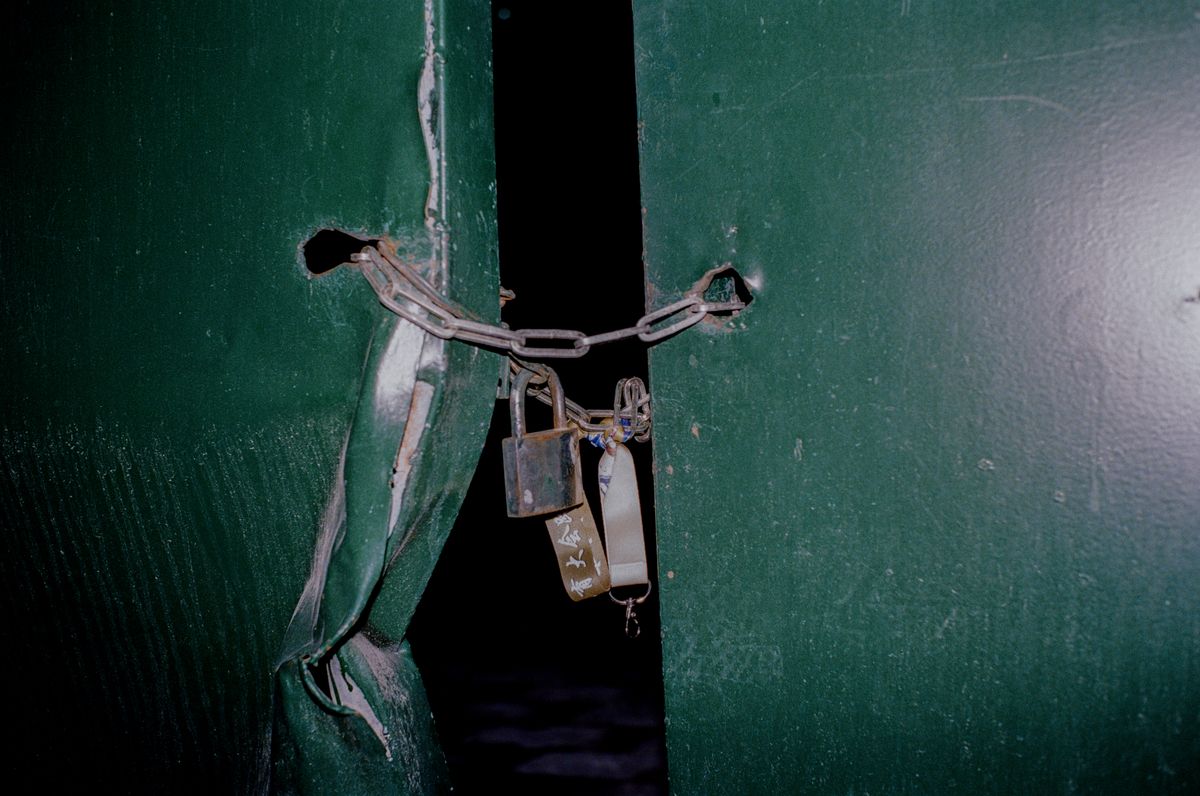 Two padlocks and a chain holding a dented green metal gate shut, with a gap still visible between the two panels.