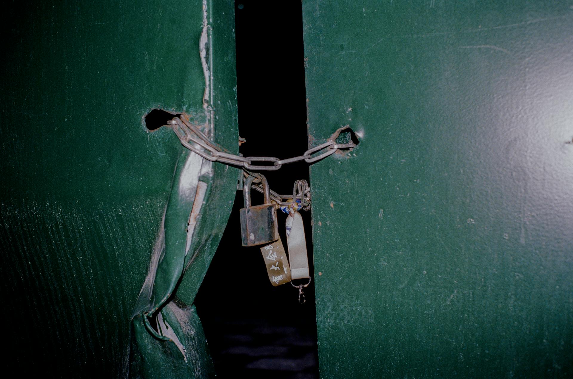 Close-up of a rusty padlock and chain securing green metal doors, blocking entry.