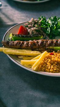 Tasty grilled kebab served with vegetables and rice on a white plate.