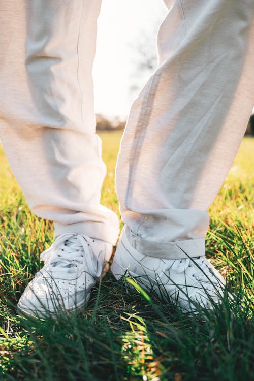 Close Up Shot of a Person in White Shoes Standing on Grass