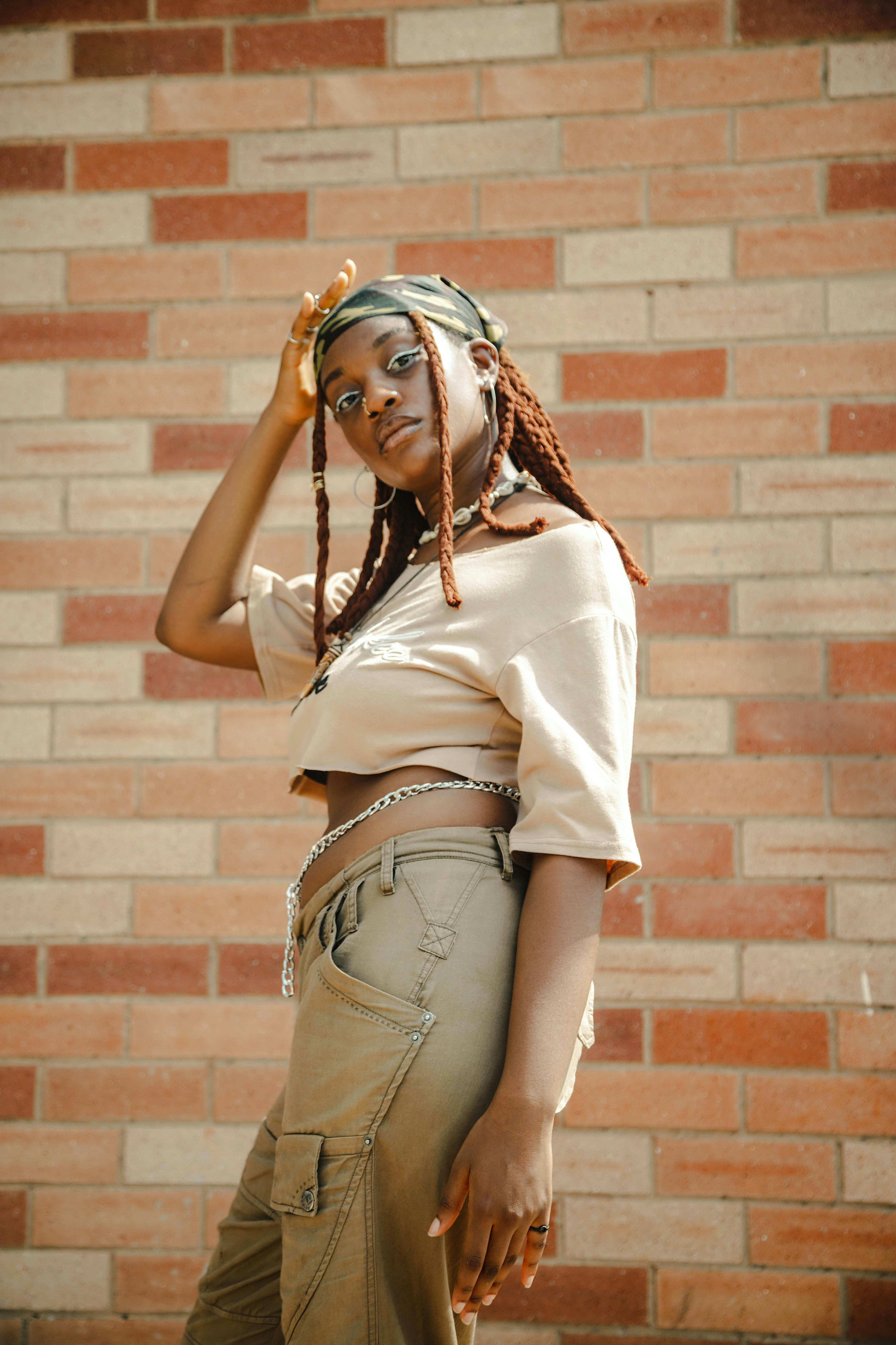 Stylish woman in crop top and cargo pants poses confidently by a brick wall.