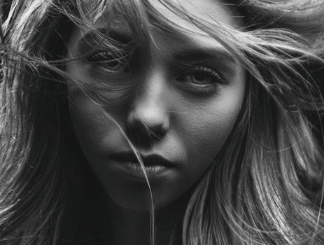Intense black and white close-up portrait of a woman with wind-swept hair.