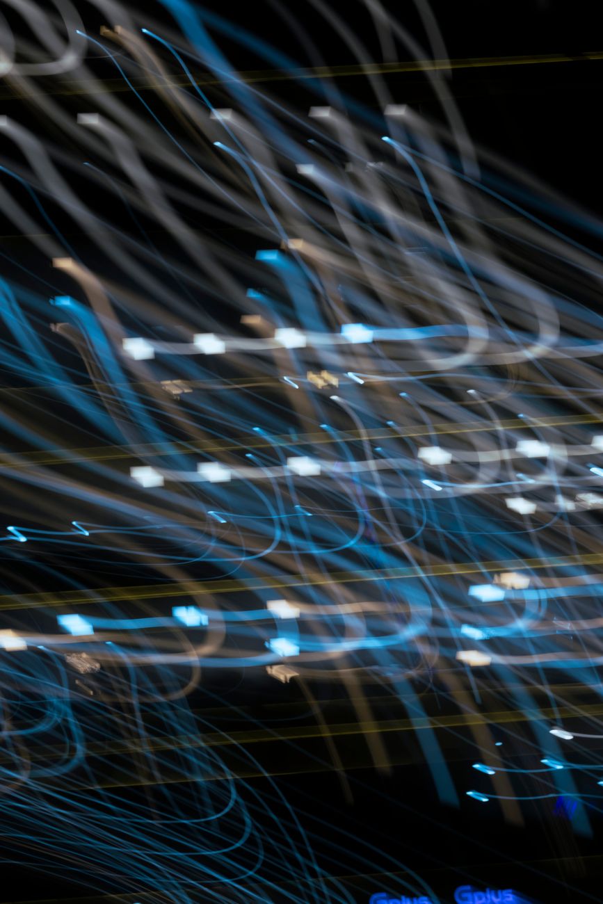 Abstract long exposure of vibrant blue and white light trails against night sky.