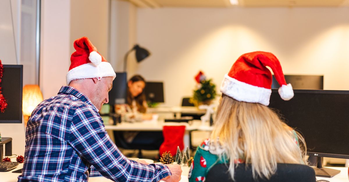 Colegas con sombreros de Papá Noel colaborando en un entorno de oficina festivo durante la época navideña.