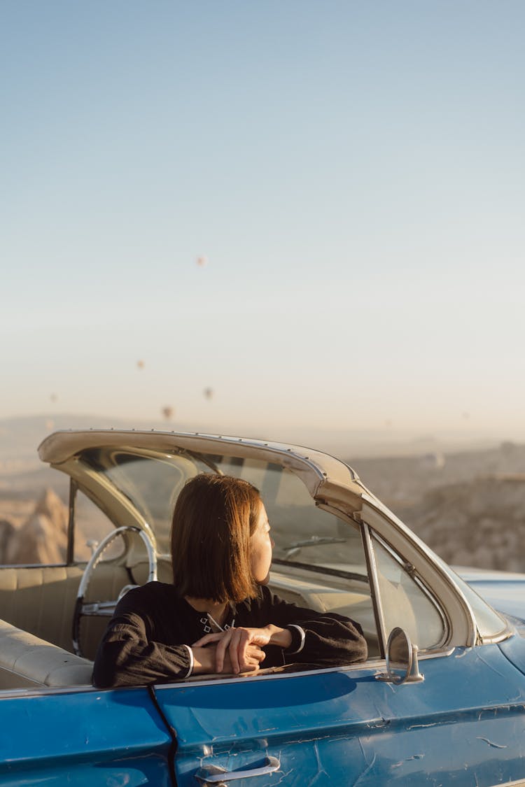 Woman Sitting In Car And Looking At Floating Hot Air Balloons