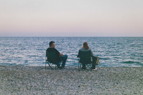 Free A couple relaxes by the ocean on camping chairs during a serene sunset. Stock Photo