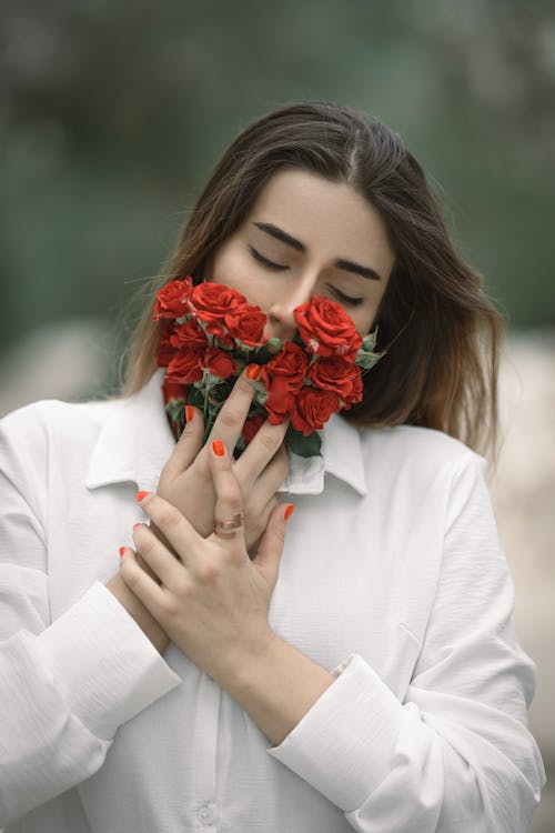 Close-Up Shot of a Beautiful Woman in White Long Sleeves Holding Red Roses