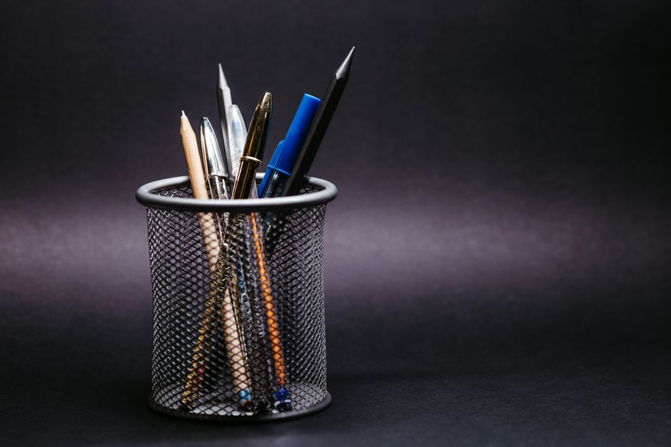 Close-up of various pens and pencils in a mesh holder against a black background.