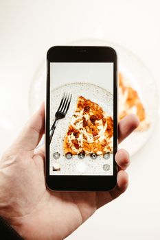 Close-up of hand photographing a pizza slice with a smartphone.