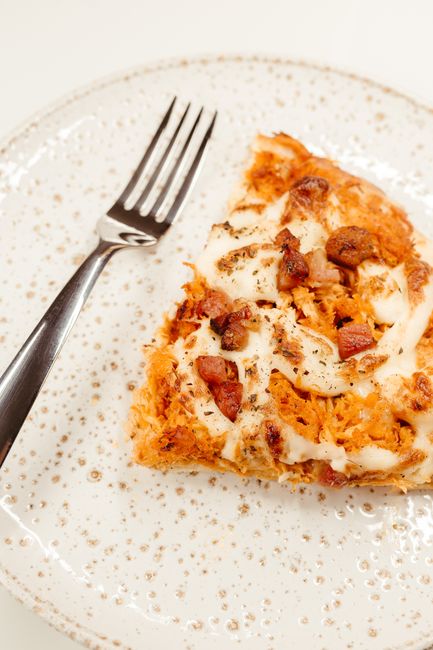 A sliced chicken bacon ranch pizza on a wooden board, topped with melted mozzarella and cheddar, crumbled bacon, shredded chicken, and thin red onion rings, with a golden crust.