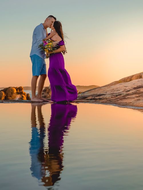 Free Couple sharing a tender moment at sunset, reflecting in calm water. Stock Photo