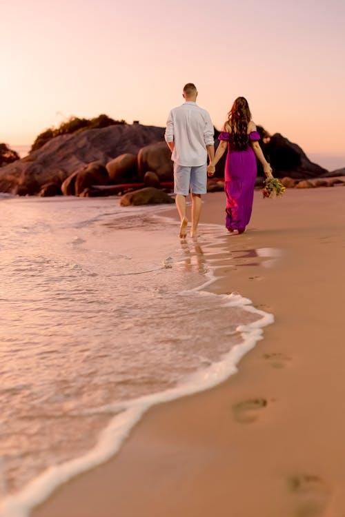 Free Couple Holding Hands While Walking on Shore Stock Photo
