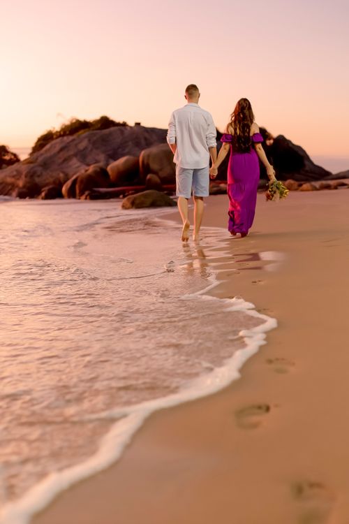 Free Couple walking hand in hand on a sandy beach during sunset, creating a romantic scene. Stock Photo