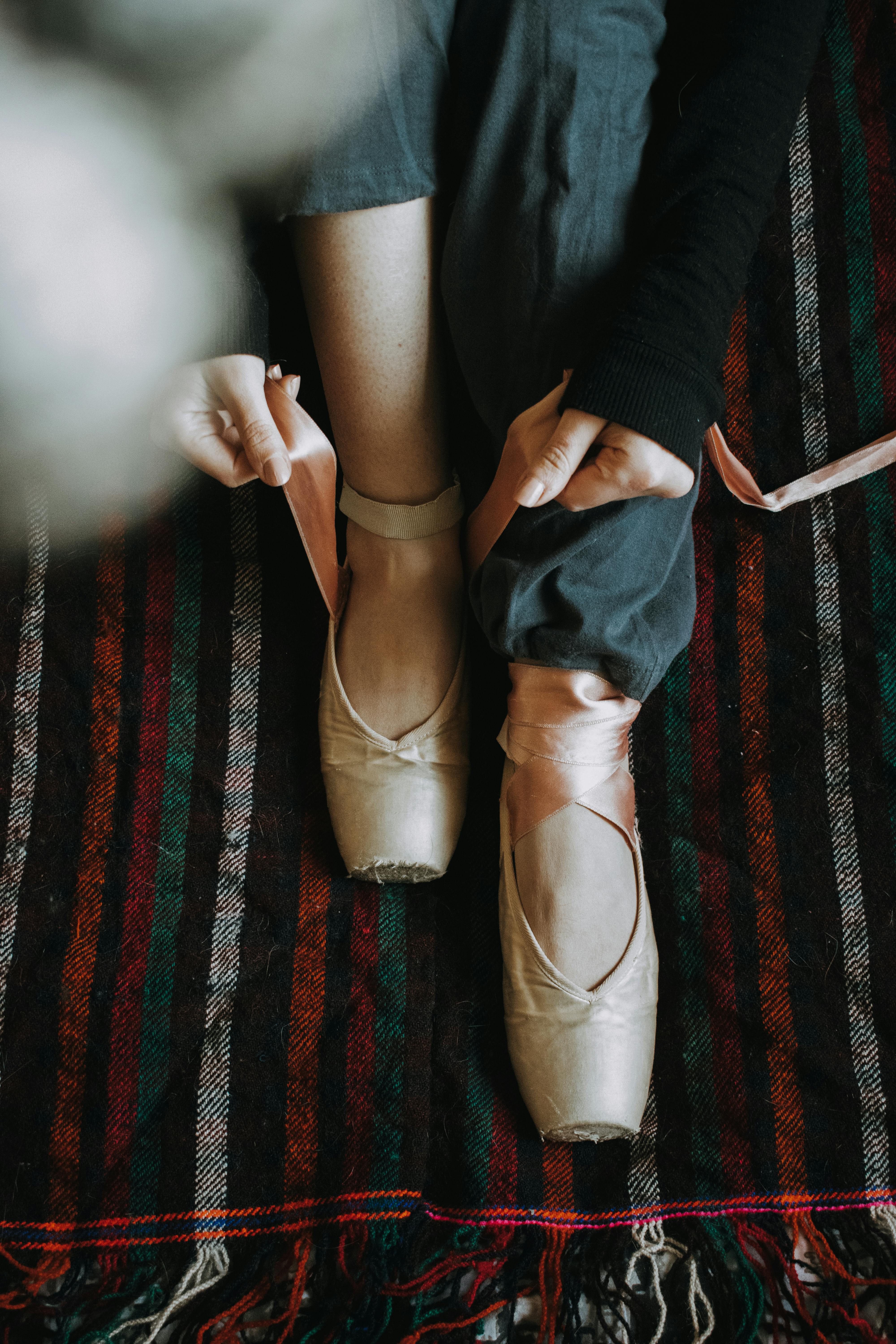 Close-up of a ballet dancer tying pointe shoes on a colorful striped carpet.
