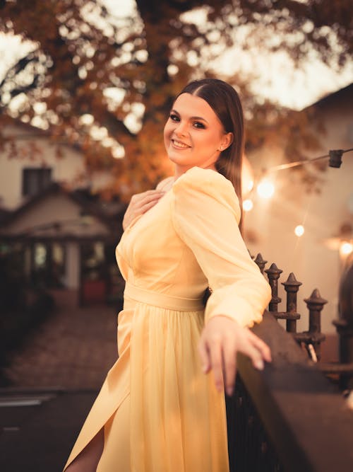 Smiling Woman in a Yellow Dress Leaning on a Railing in a Park