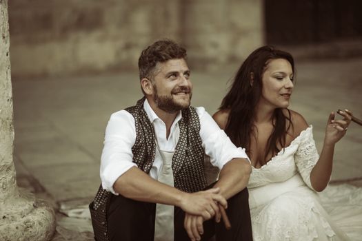 A romantic couple sitting together outdoors in elegant, stylish attire, enjoying a moment.