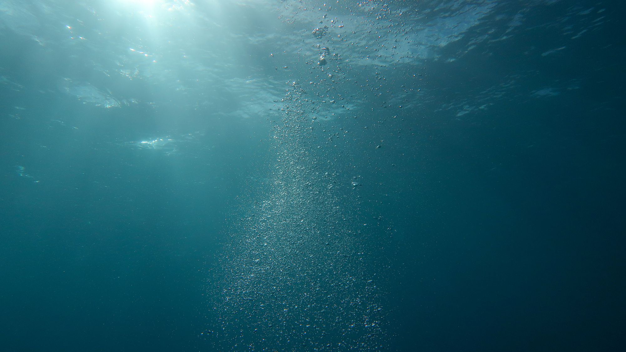Rayos de luz atravesando el agua azul del océano con burbujas que ascienden hacia la superficie