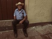 An elderly man in a cowboy hat sitting on an outdoor step, offering a candid street photography feel.