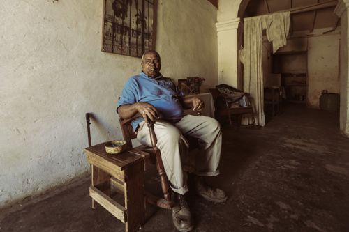 Free Elderly man in blue shirt sits thoughtfully indoors in a rustic room, exuding a warm, nostalgic vibe. Stock Photo