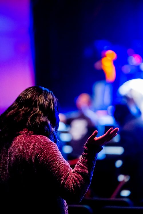 Free A woman with raised hand in a dim venue, capturing spiritual ambiance and vivid lighting. Stock Photo