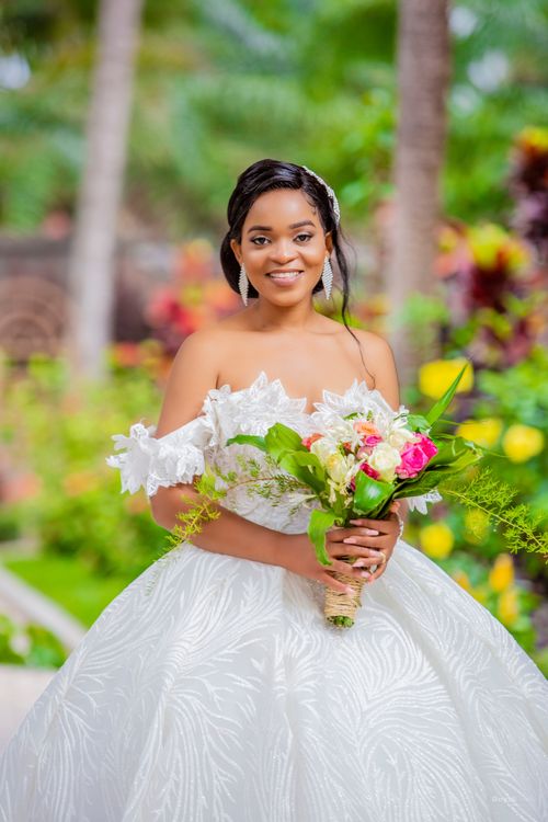 Free Joyful bride in a stunning dress holding a bouquet, surrounded by lush greenery on her wedding day. Stock Photo