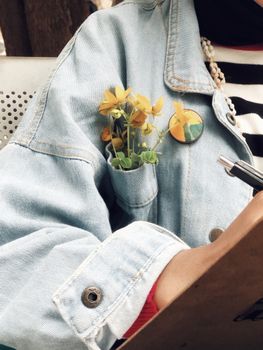 Close-up of a denim jacket with yellow flowers in the pocket, offering a stylish and vibrant look.