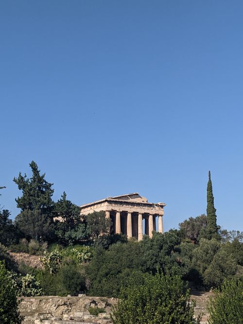 Free Scenic view of the Temple of Hephaestus in Athens surrounded by lush greenery under a clear blue sky. Stock Photo