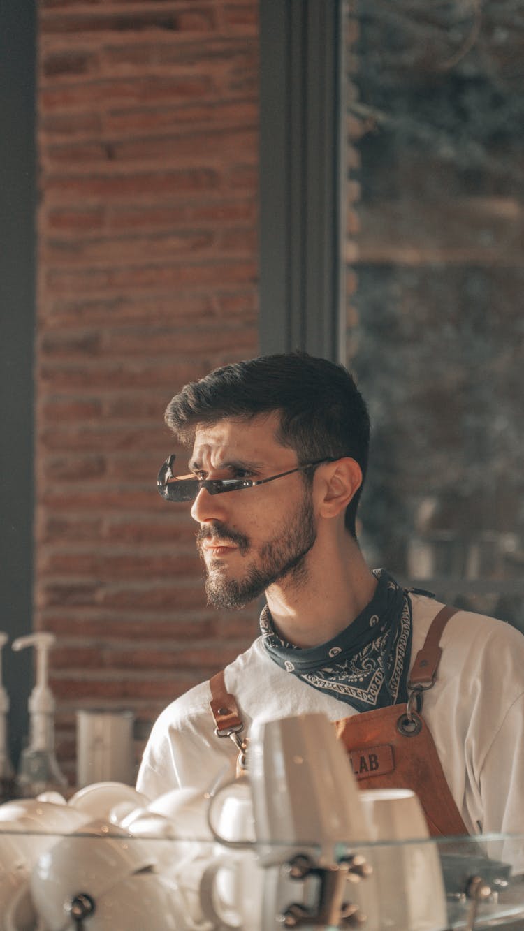 Man In An Apron And Sunglasses Behind A Stack Of Mugs