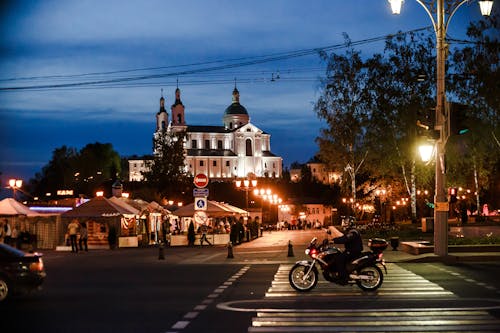 Person on a Motorcycle on a Street in City with Illuminated Buildings in the Evening 
