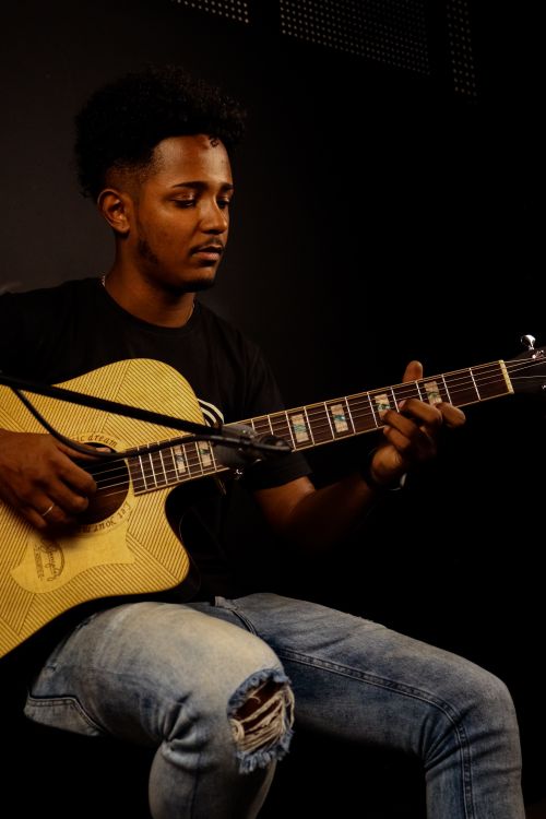 Free A young African American man skillfully playing an acoustic guitar in a dimly lit room. Stock Photo