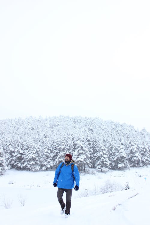 A Man in Blue Jacket Walking on Snow Covered Ground