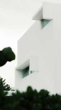 A minimalist modern building with white concrete exterior set against a cloudy sky.
