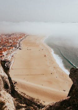 A stunning aerial view of Nazaré Beach with red roofs and fog rolling in, capturing the town's charm.