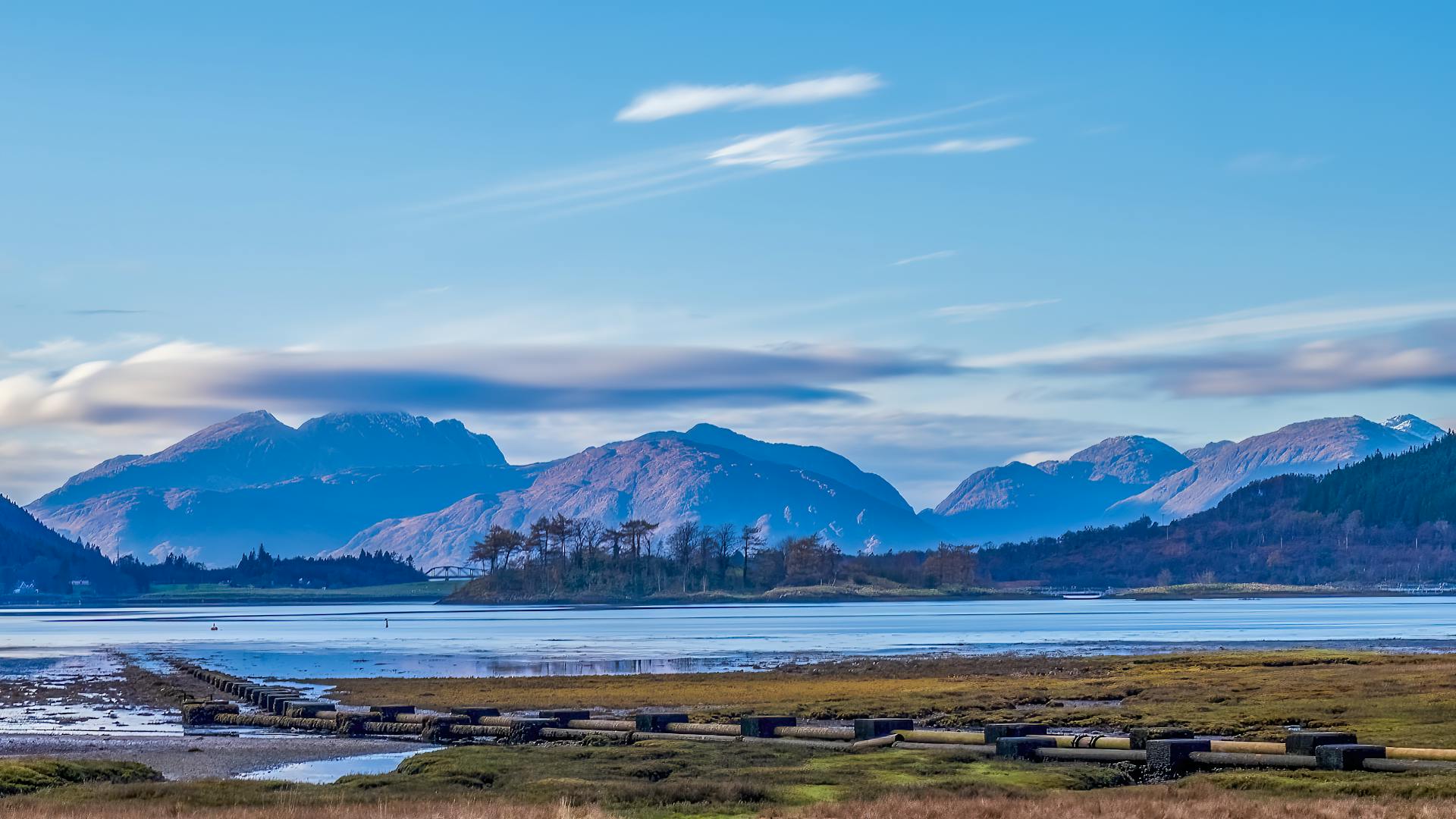 Picturesque mountain lake view with blue skies and pipelines in the foreground.