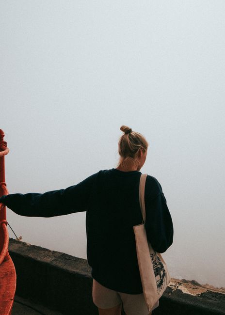 A woman stands by a railing in foggy Nazaré, Portugal, overlooking the sea.