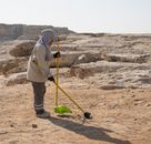A person cleaning sand near rocky formations during the day, showcasing a desert landscape.