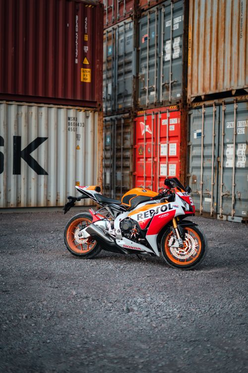 Free Colorful sport motorcycle parked by cargo containers in an industrial setting. Stock Photo