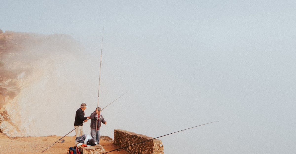 Photo by Artūras Kokorevas Two fishermen on misty cliffs in Nazaré, Portugal, capturing a peaceful seaside moment.