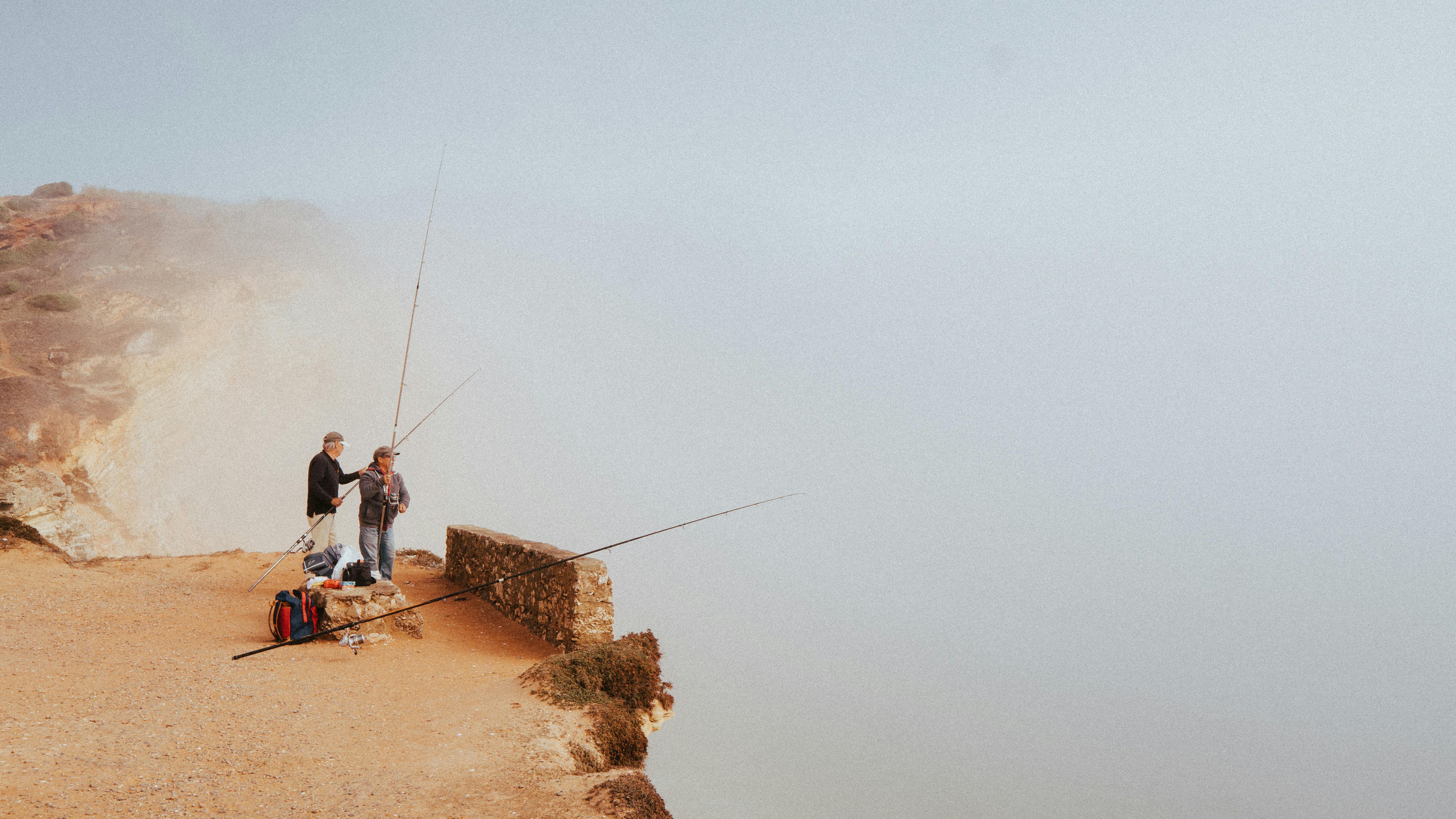 Two men fishing on a foggy cliff in Nazaré, Portugal, creating a serene and misty scene.