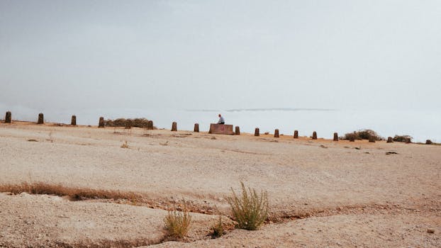 A lone person sitting near a stone barrier amidst a misty coastal view in Nazaré, Portugal.