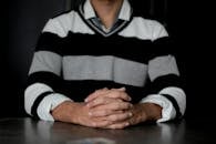 一名男子身穿条纹毛衣，双手交叉坐在室内的桌子上
