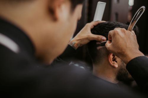 Free Close-up of a barber expertly styling a man's hair with a razor and comb in a trendy barbershop. Stock Photo