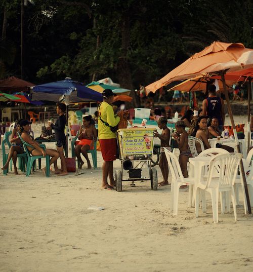 Free A lively beach scene with tourists, colorful umbrellas, and a food vendor in Madre de Deus, Brazil. Stock Photo